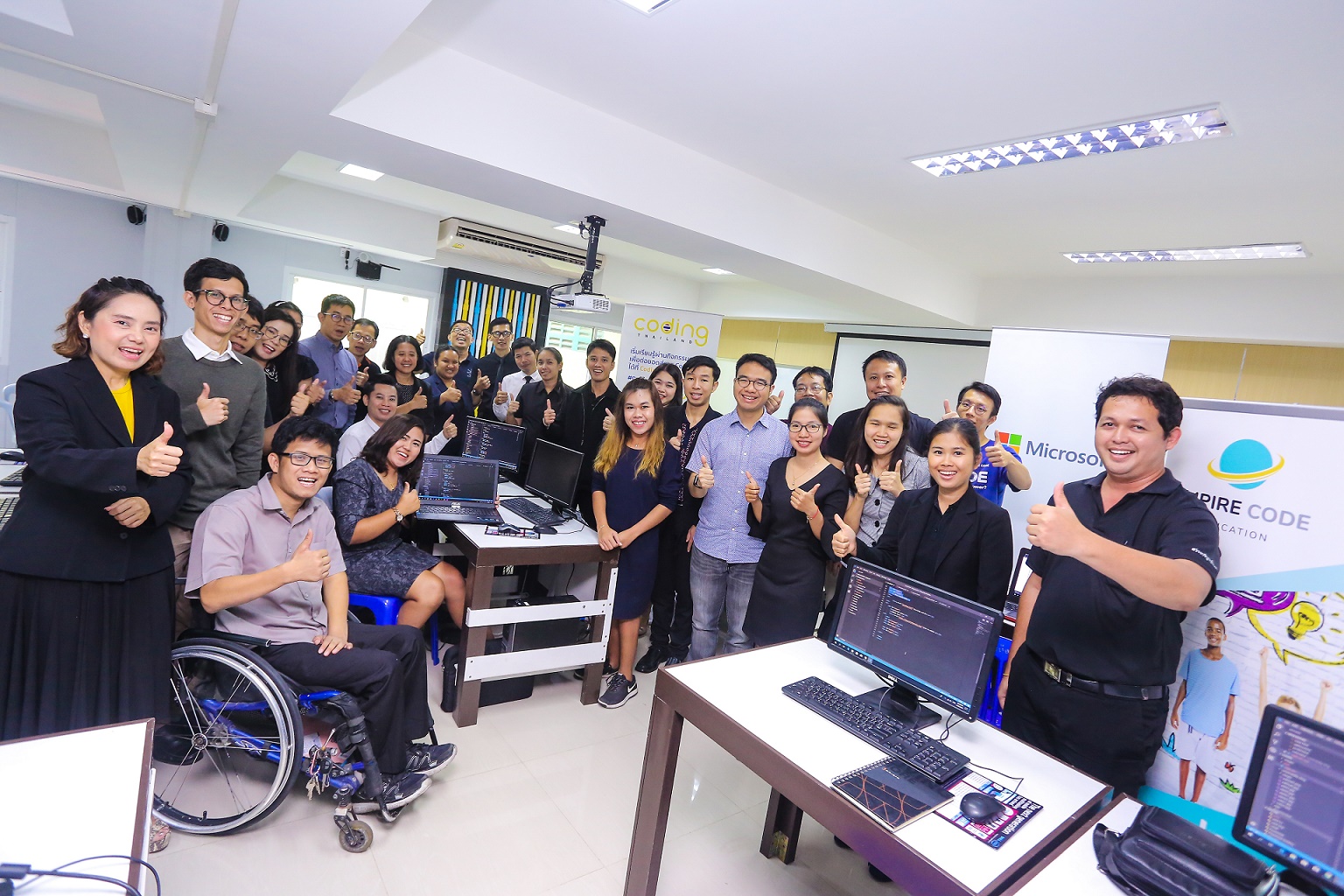 Group of men and women doing thumbs-up gesture with in room with computers
