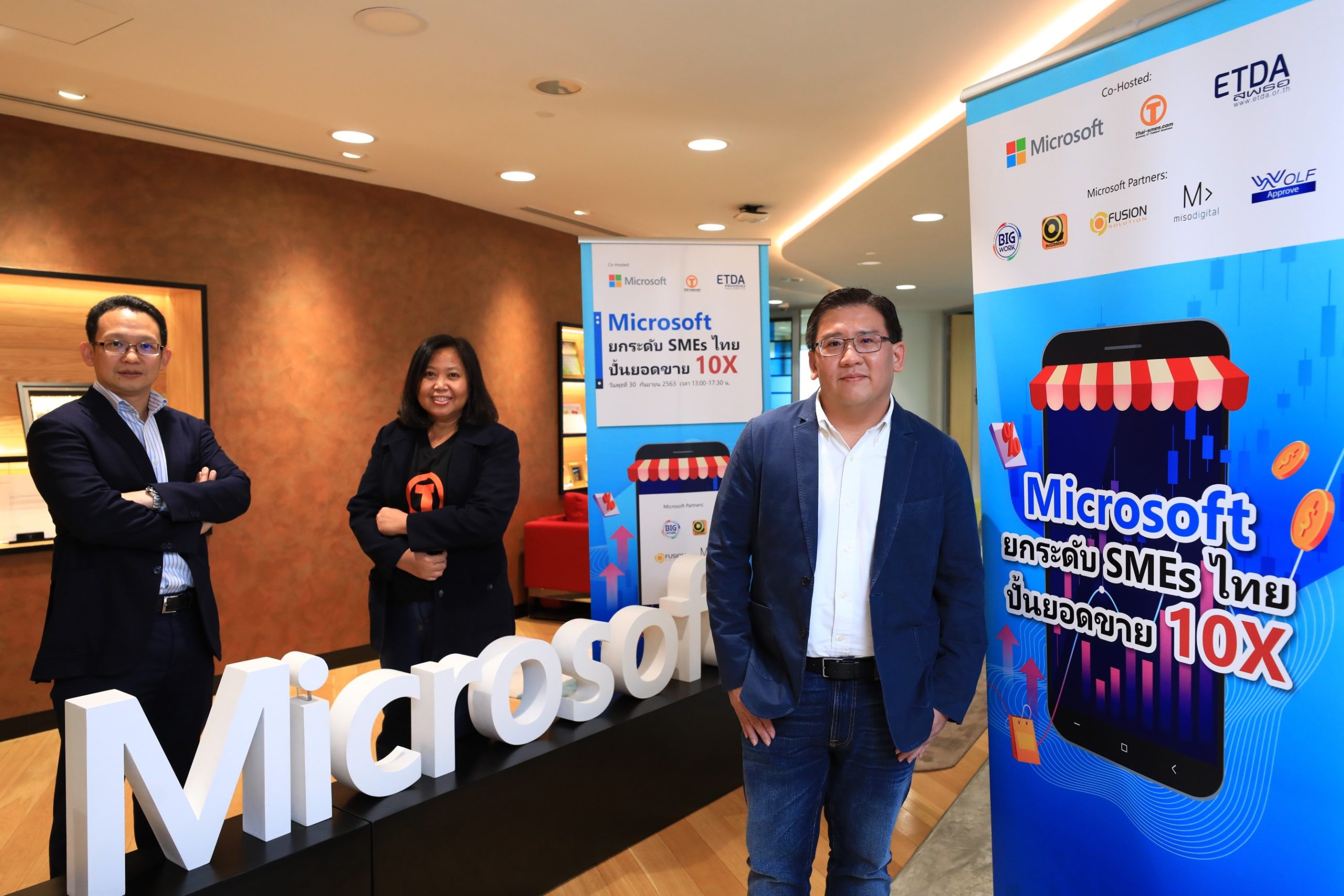 Three people with Microsoft logo and Thai SME event signage