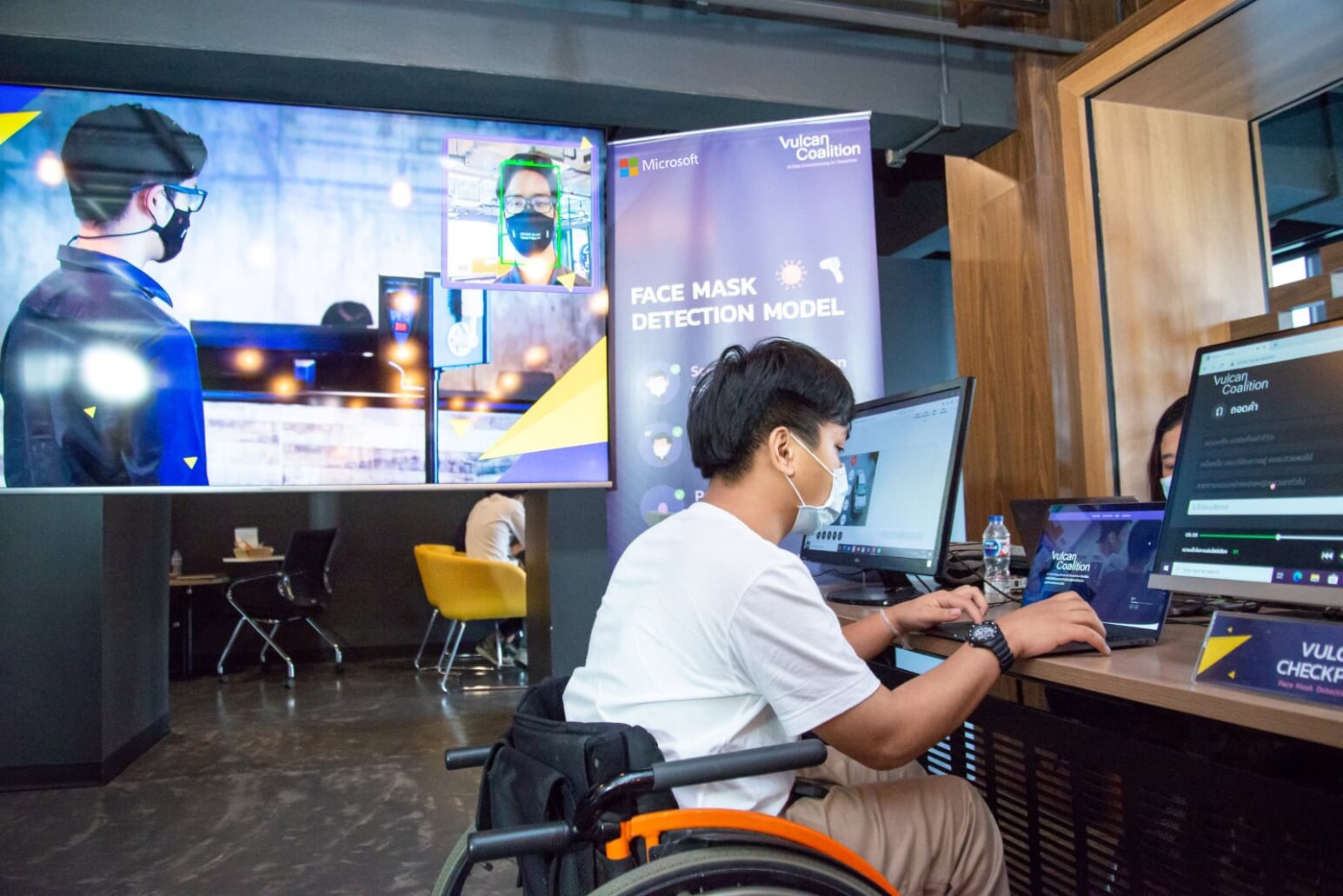 Man in wheelchair using a laptop in front of demo TV screen