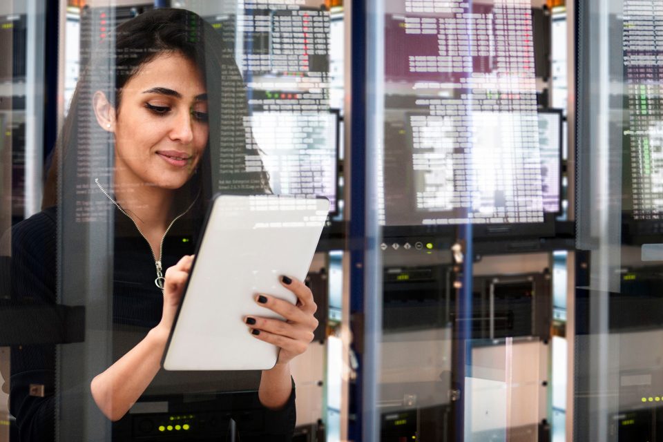 Woman using a tablet behind glass window with reflections of screens