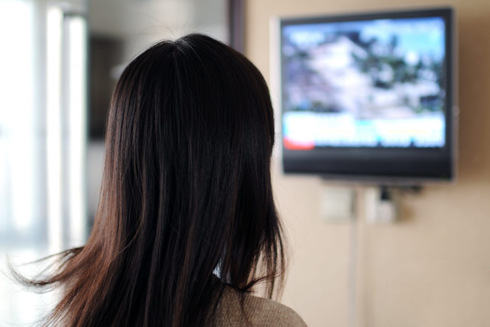 字幕のテレビを見ている女性の後ろ姿