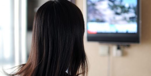 字幕のテレビを見ている女性の後ろ姿