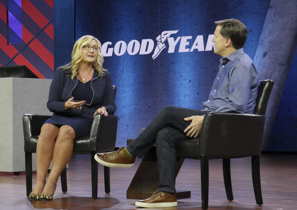A woman and a man sit in chairs on stage talking.