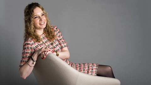 Jasmin Fisher reclines on a chair, smiling off into the distance