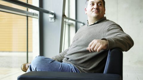 Cedric Fournet sits in a chair, looking over his shoulder, in front of a glass wall