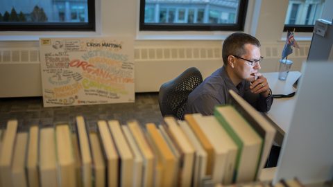 Duncan Watts sits deep in thought looking at his computer in his office surrounded by books