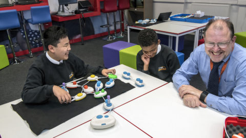 Daniel and Rico sit smiling at a table with a string of plastic pods, also with a smiling Jonathan Fogg