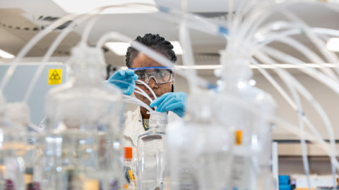 A woman handles plastic tubes and glass jars in a lab