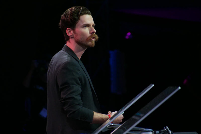 A man stands on stage presenting in front of a computer