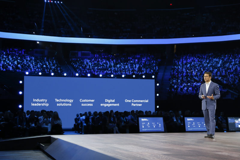 A man stands on stage in front of a screen presenting.