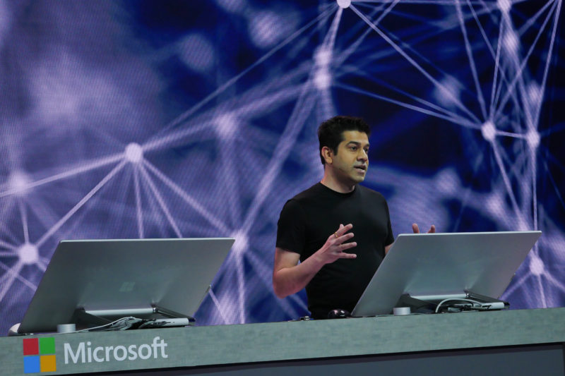 A man stands on stage behind a podium demonstrating a computer product