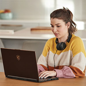 A woman sits at kitchen table working on computer