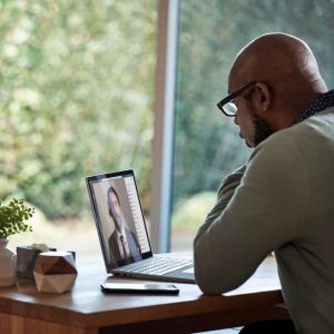 a man works at a laptop in front of a window in his home