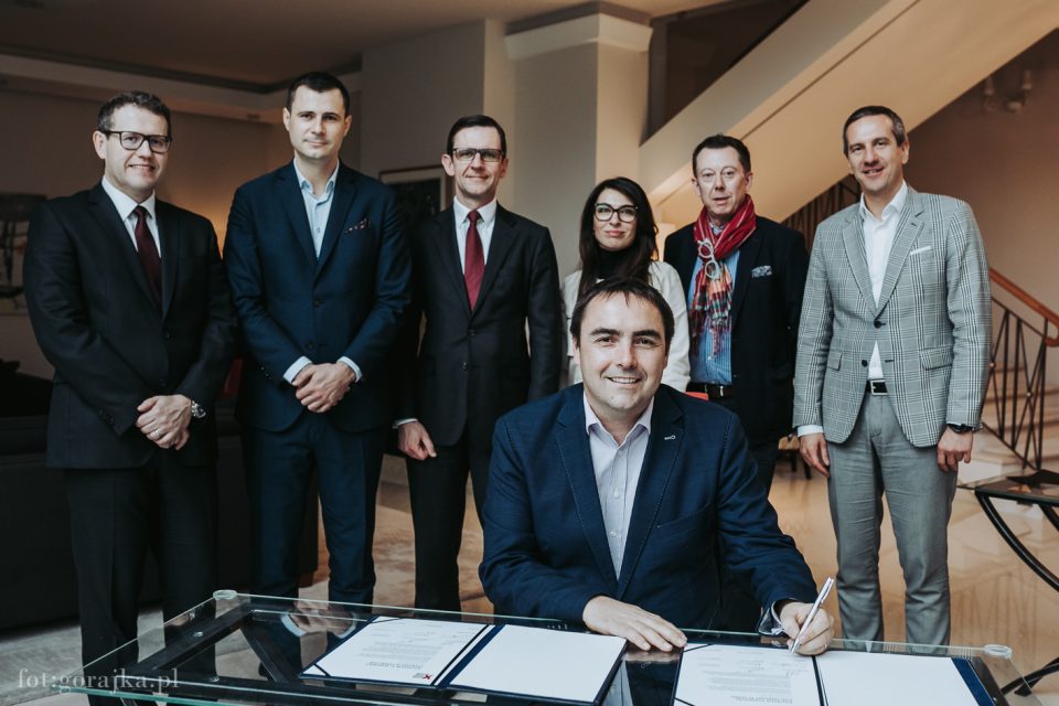 group of people standing behind a person signing document