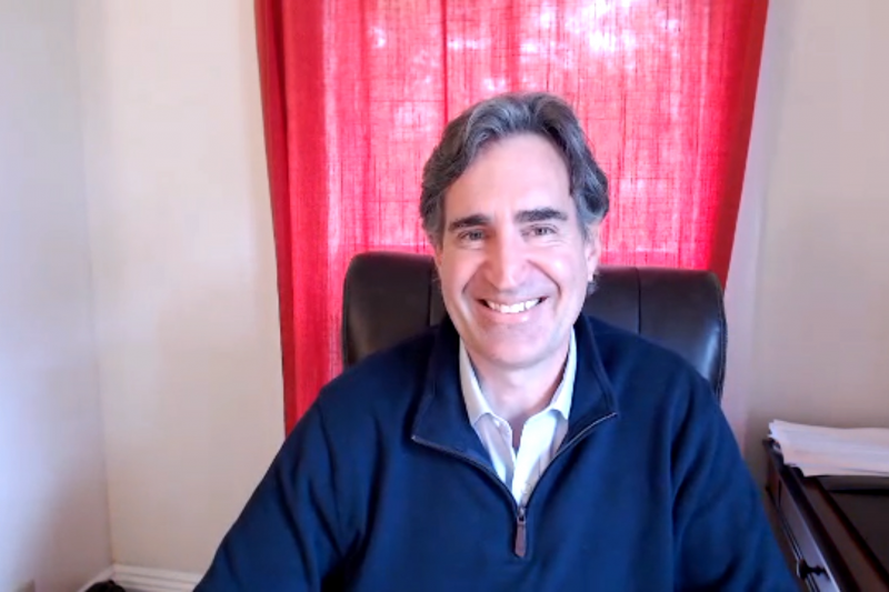 Man in blue pullover with red curtains in background