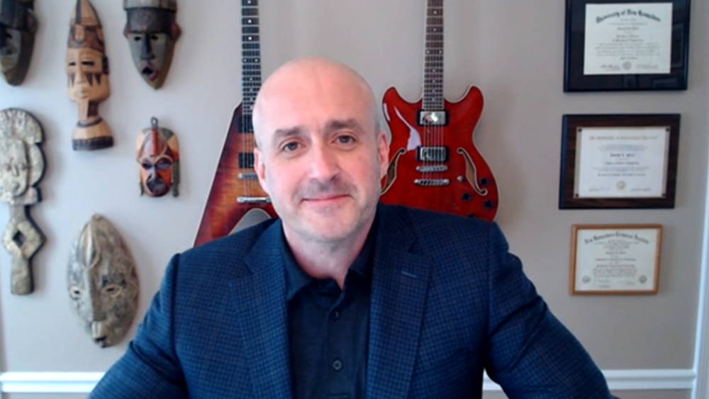 Man in navy suit with guitars on wall in background