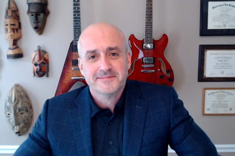 Man in navy suit with guitars on wall in background