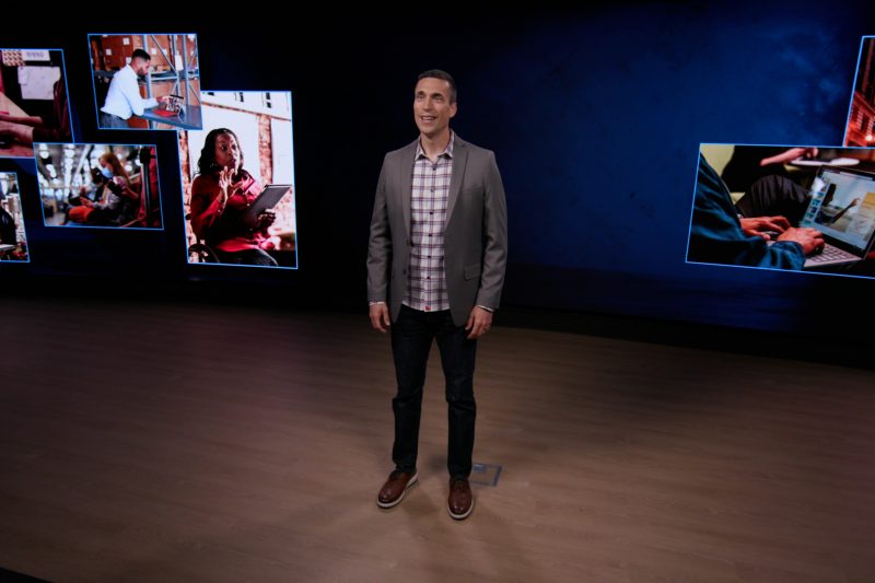 Jared Spataro standing in a room with screens behind him