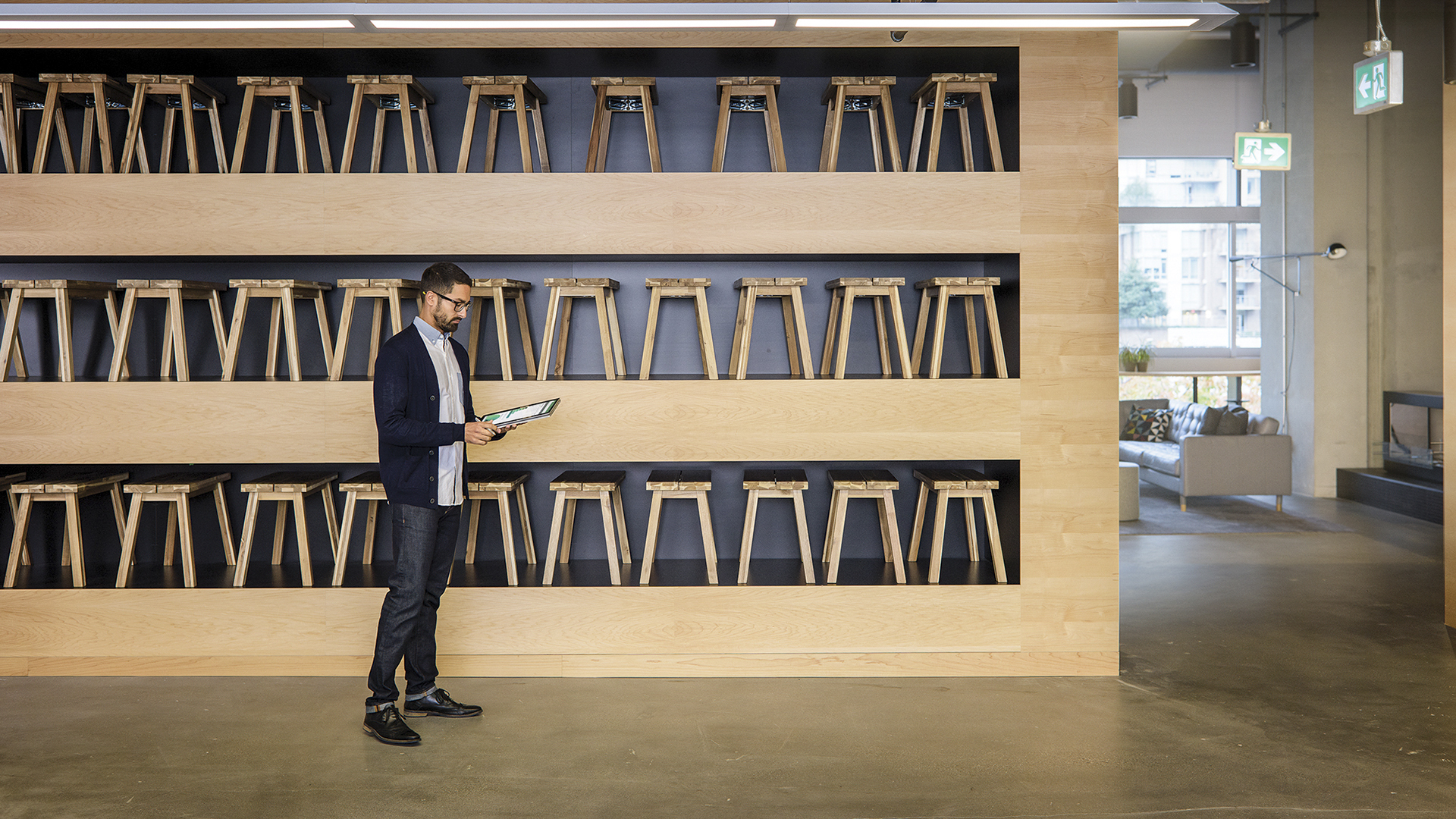 Person holding a tablet in front of a showcase of wooden stools