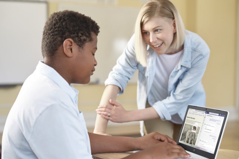A boy uses a laptop as a woman talks to him