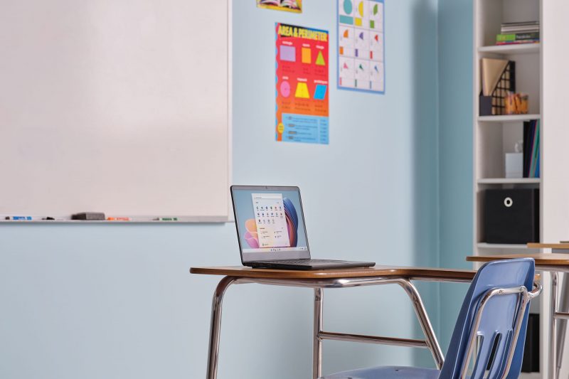 A laptop sits on a desk in a classroom