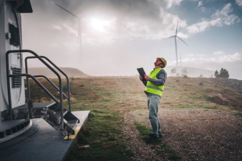 A man stands outside looking towards the sky with a vest and hard hat on