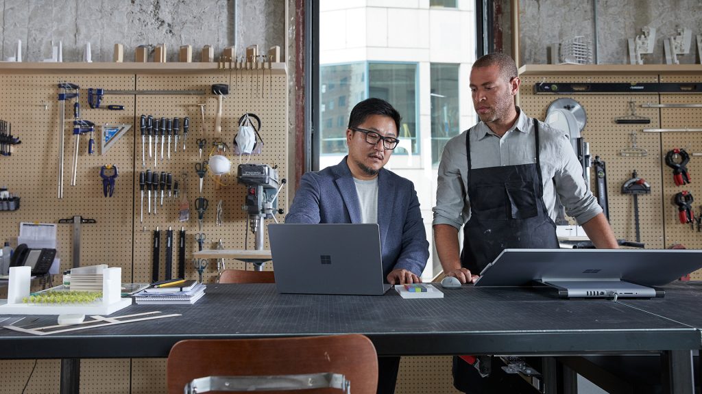 Two men standing working on their computers