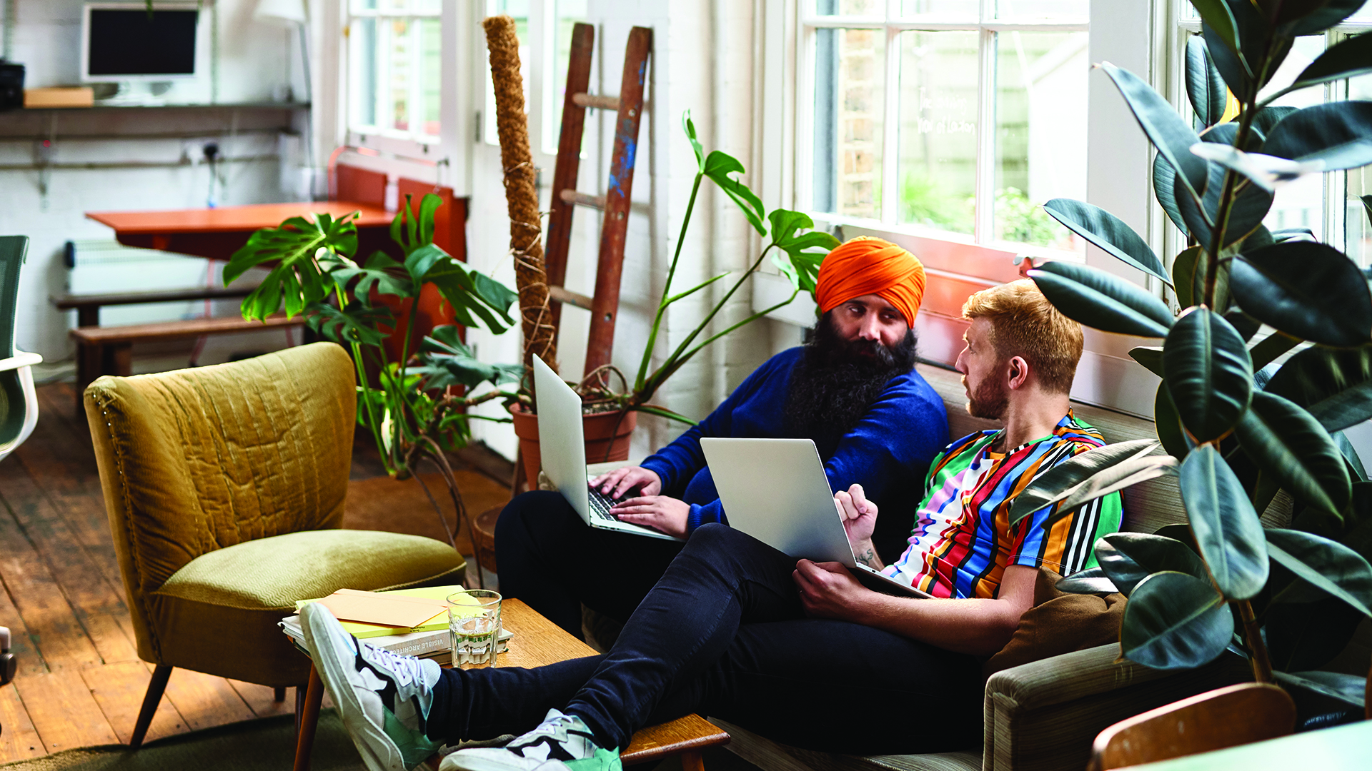 Two men sitting on a couch with laptops