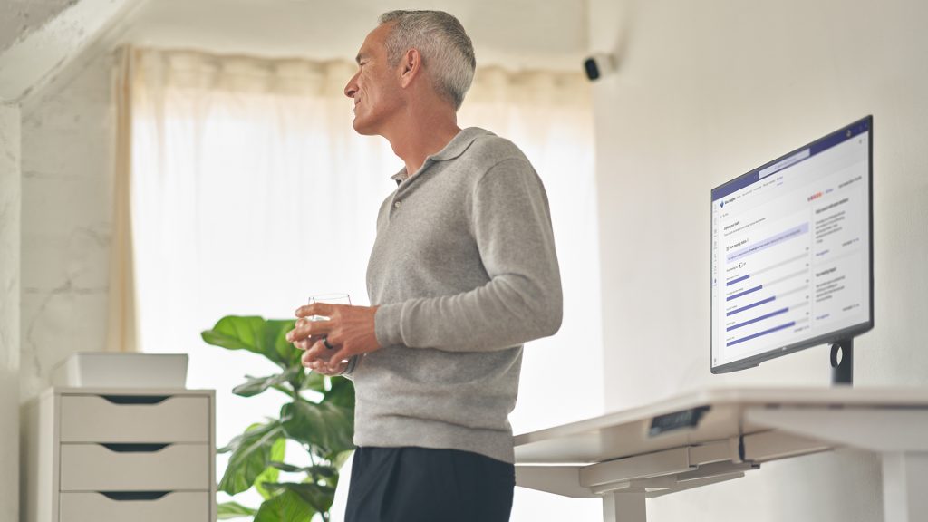 A man leans against a computer desk holding a glass