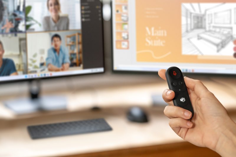 A person holds a device in front of their two computer screens while on a video call.