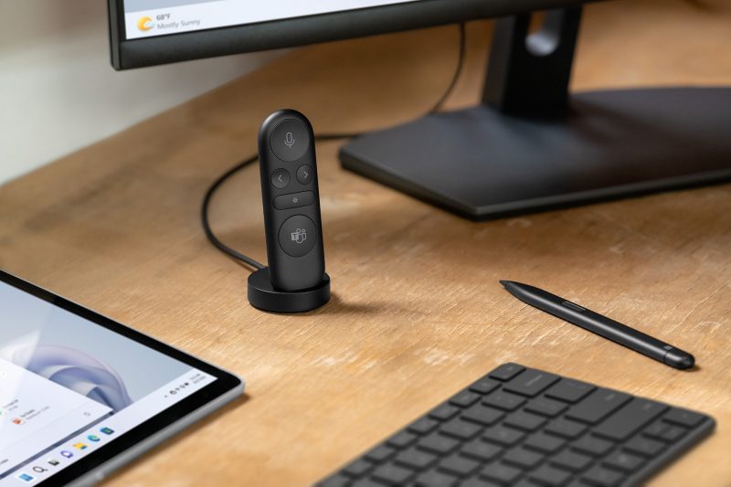 A presenter device sits inside a charging cradle surrounded by a laptop screen, computer monitor, digital pen and keyboard.