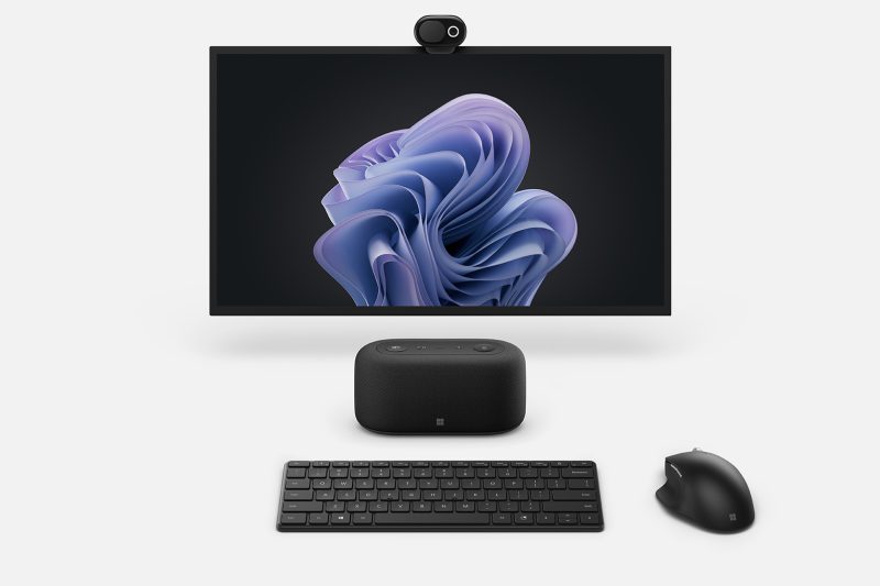 An audio dock is shown in between a keyboard with mouse and computer monitor with a webcam.