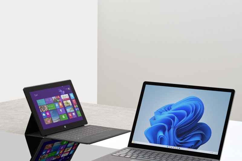 A tablet computer sits next to a laptop computer on a table.