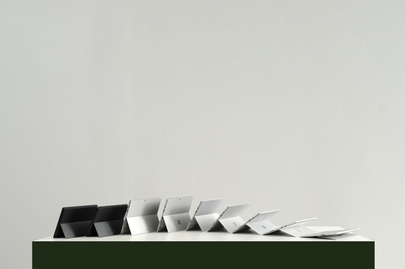 A series of nine tablet computers with kickstands are postioned next to each other on a table with each kickstand positioned slightly further back the the previous to create a wave effect.