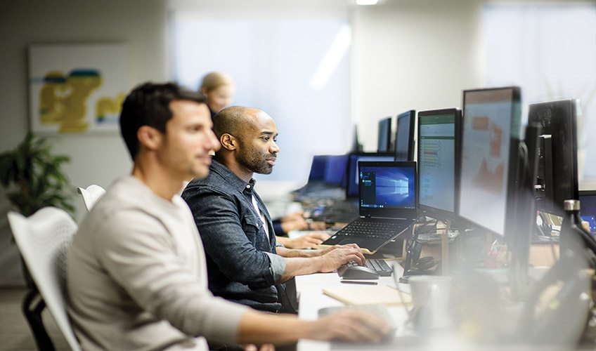 two men sitting at a desk working on computers