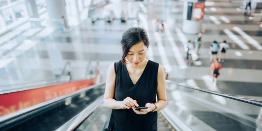 Young businesswoman reading emails on smartphone while riding on escalator