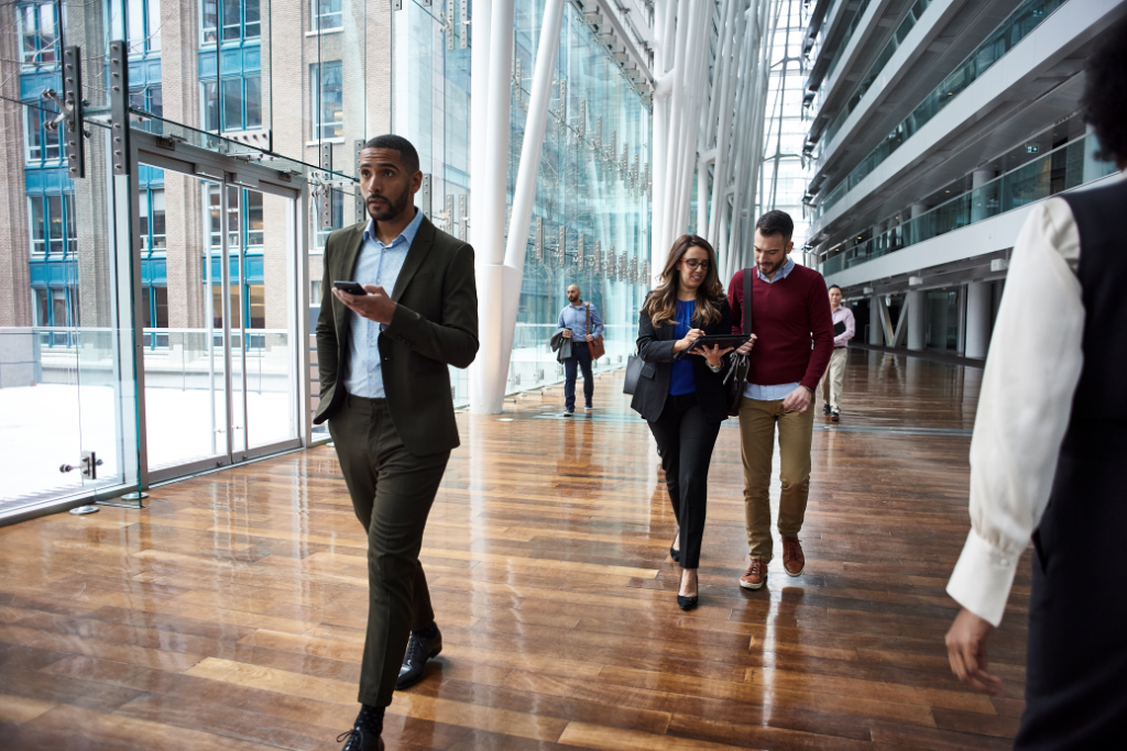 Male and female business professionals walking in large foyer on mobile deivces