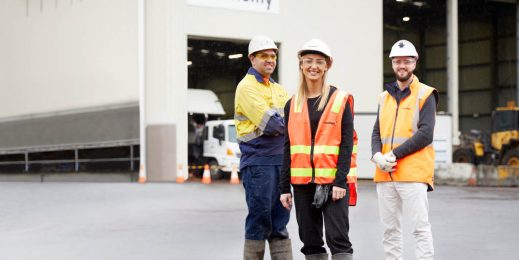 Three adults in safety gear infront of a warehouse building