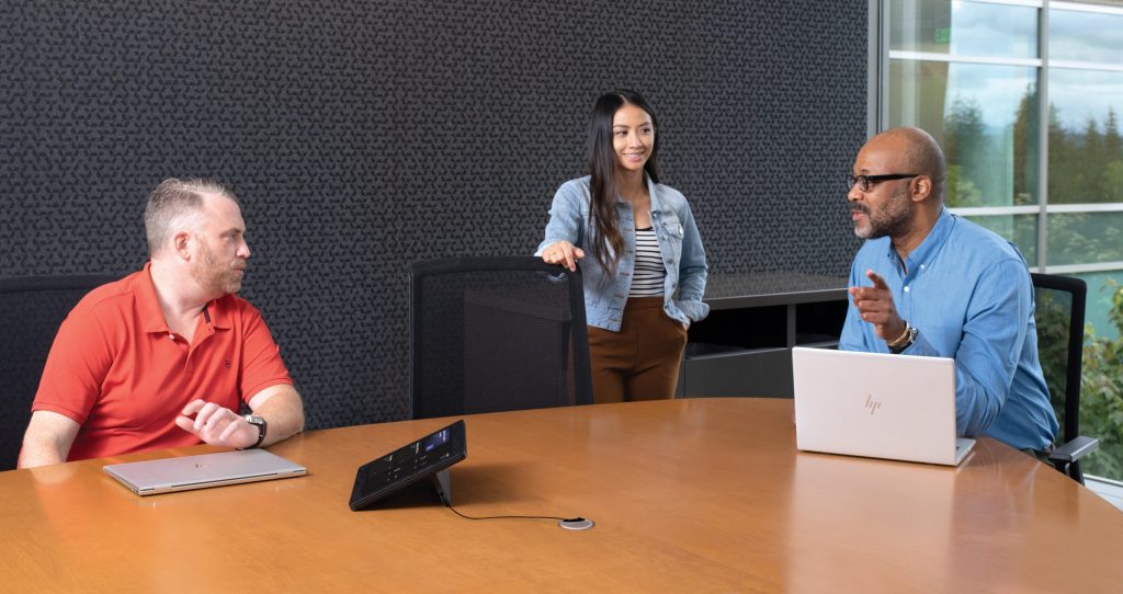 One female and two males in medium conference room with an HP Slice Microsoft Teams Rooms touch display and two HP laptops in view.