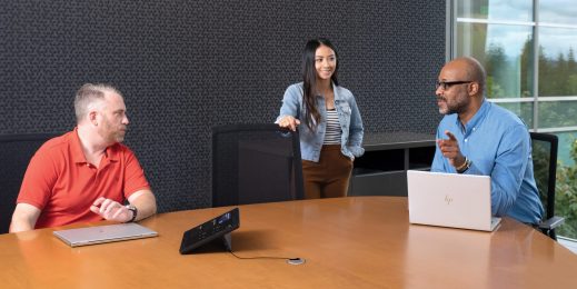 One female and two males in medium conference room with an HP Slice Microsoft Teams Rooms touch display and two HP laptops in view.