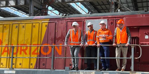 A group of adults wearing safety uniforms standing infront of a freight rail operator