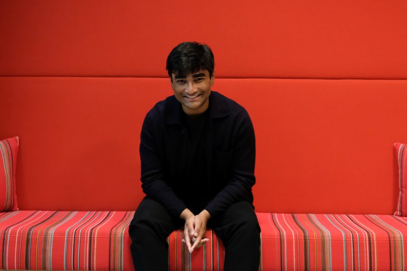 Smiling man seated on couch with red background