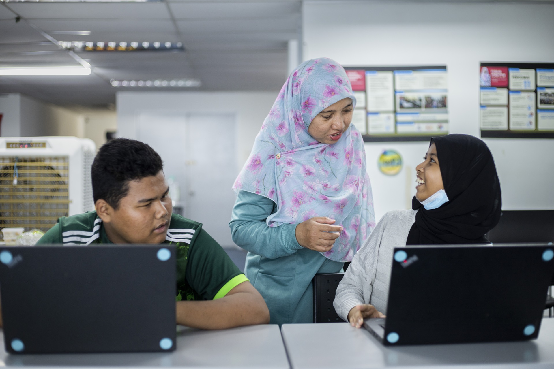 A man and two women in headscarves in conversation at their laptops