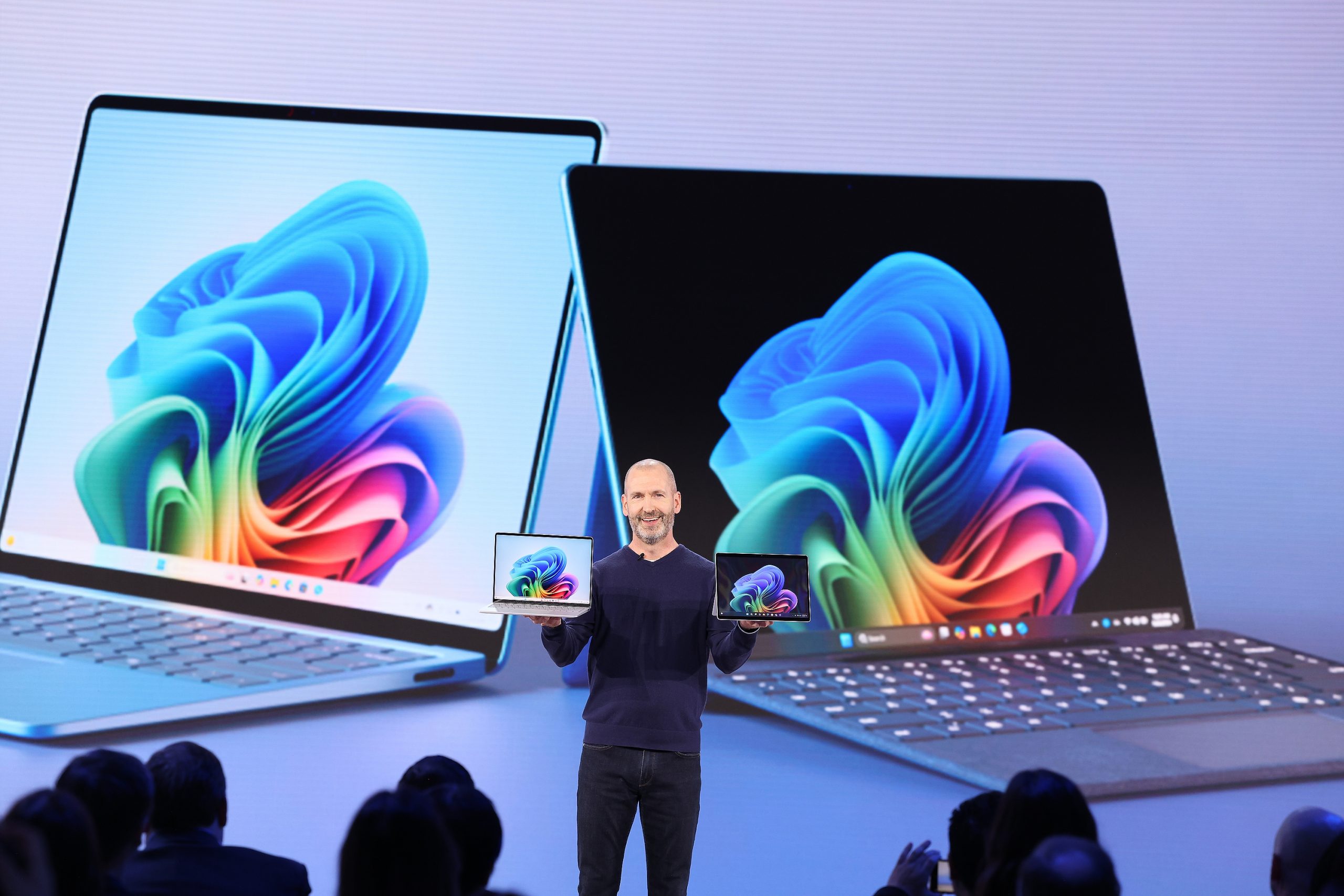 A man standing on stage in front of an audience holding two Copilot+ PCs