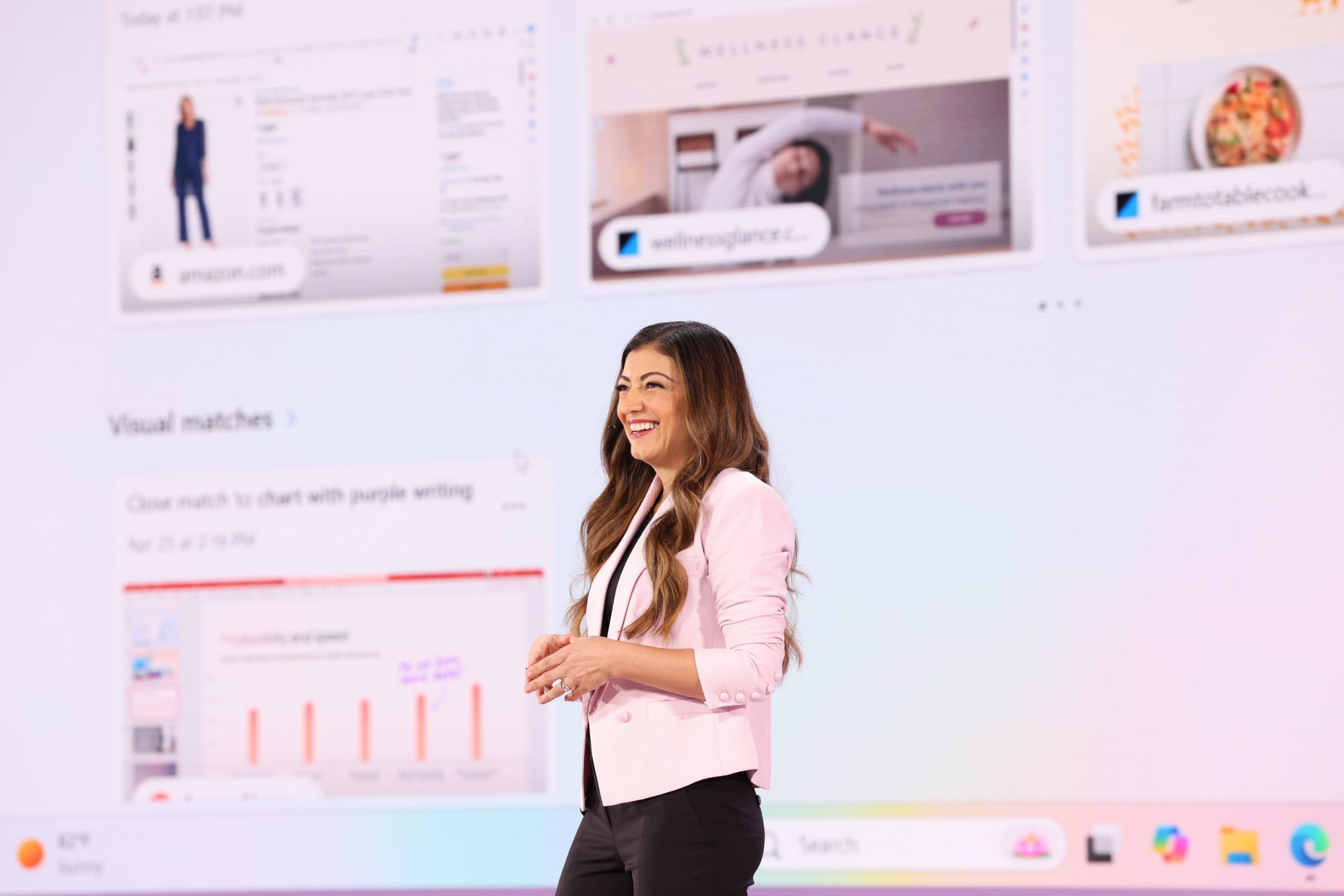 A woman standing on stage in front of an audience, with a device user interface projected on the screen behind her