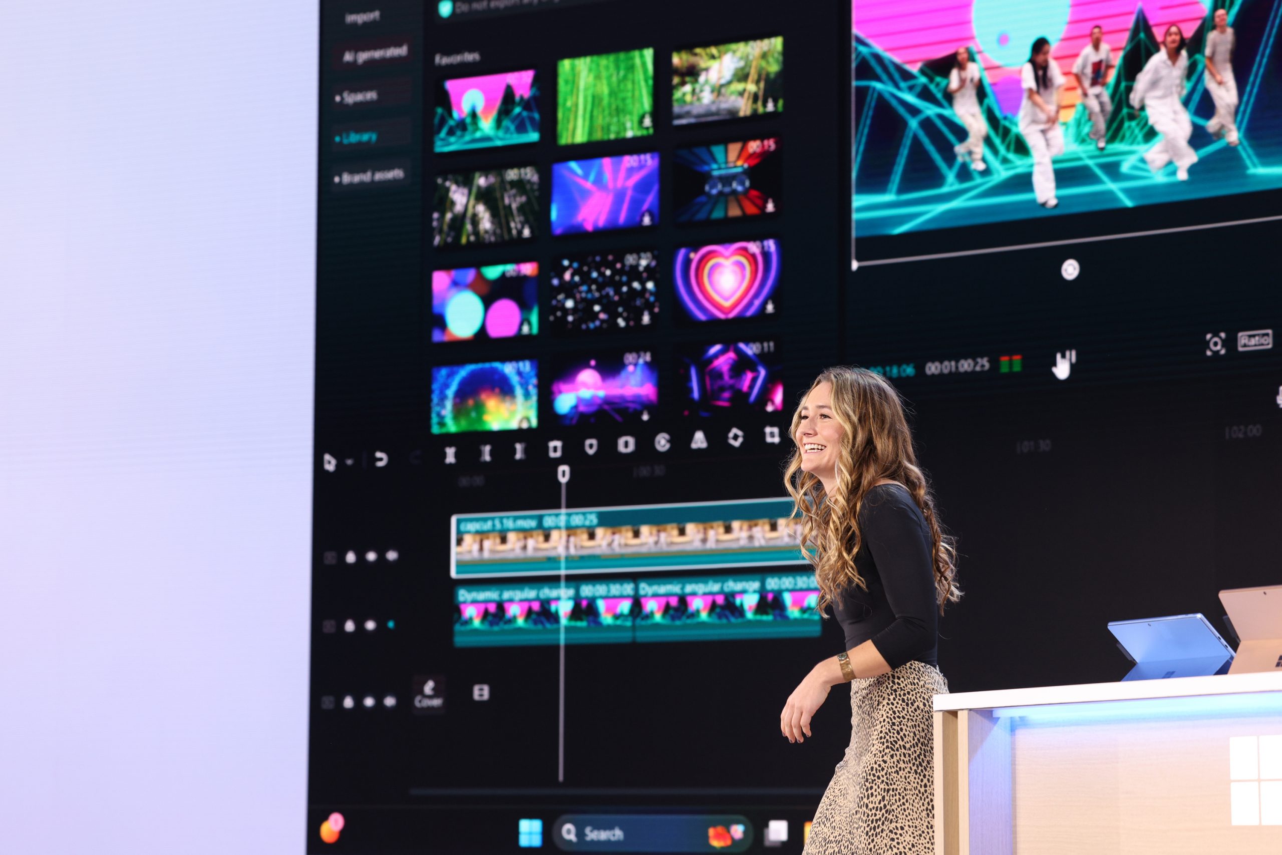 A woman standing on stage in front of an audience with a collage of photos on the screen behind her