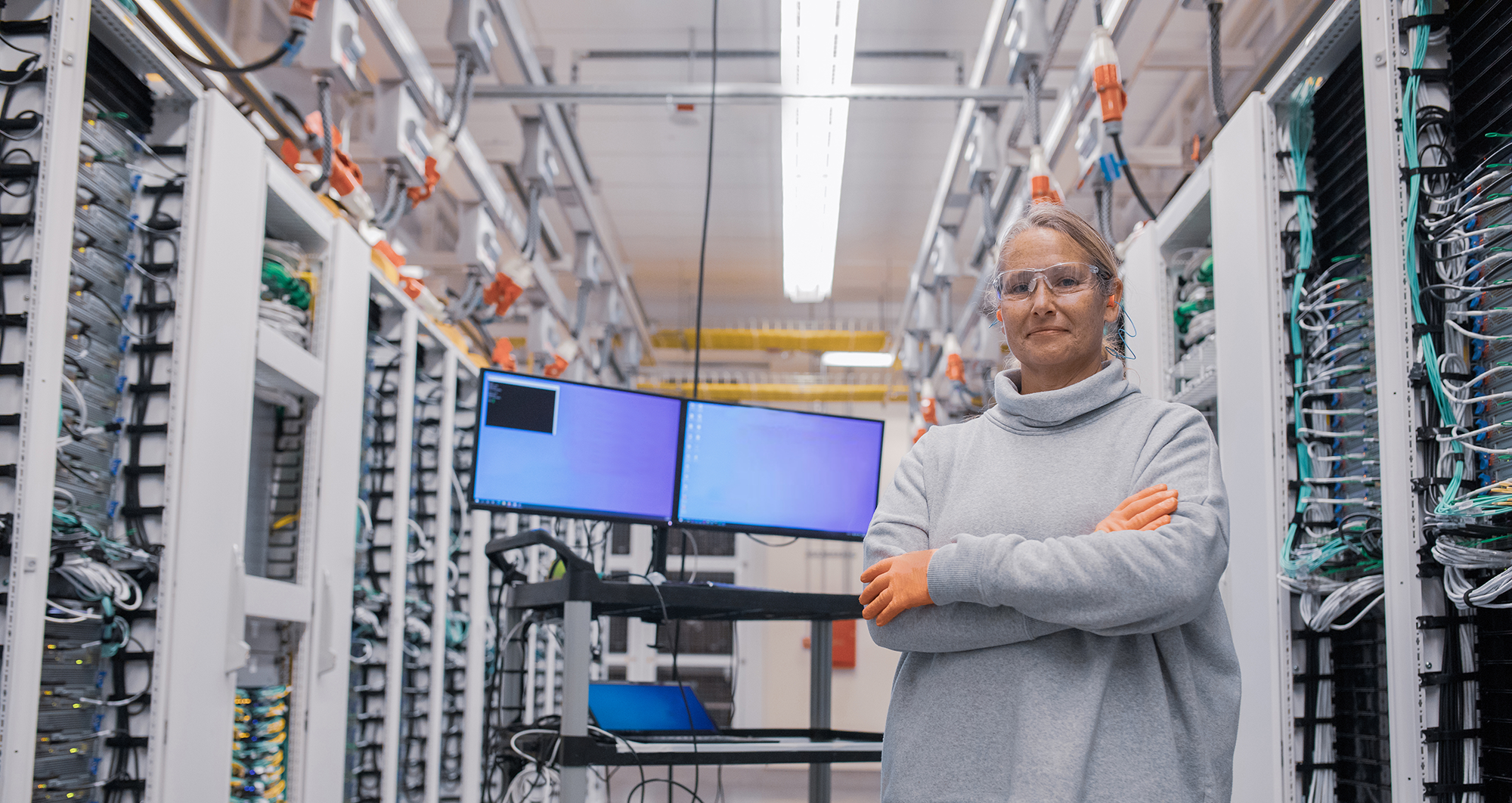 Woman stands with arms folded near a monitor