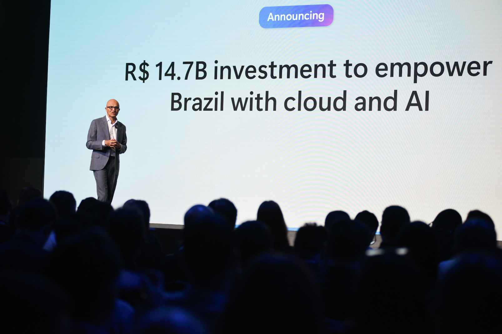 Um homem está no palco com uma grande tela projetada atrás dele