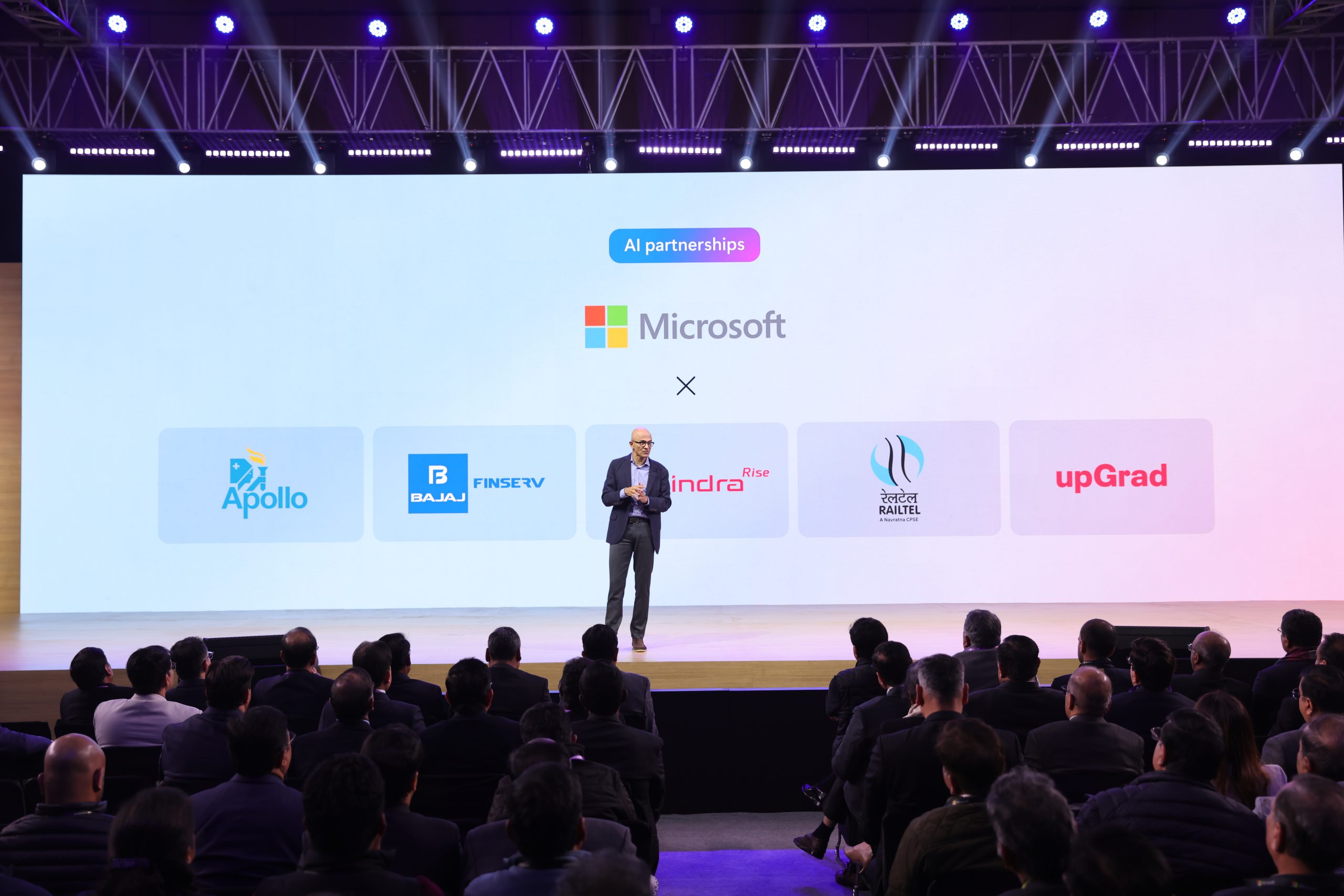 Man on stage with backdrop that reads AI partnerships and then the microsoft logo with other brand logos