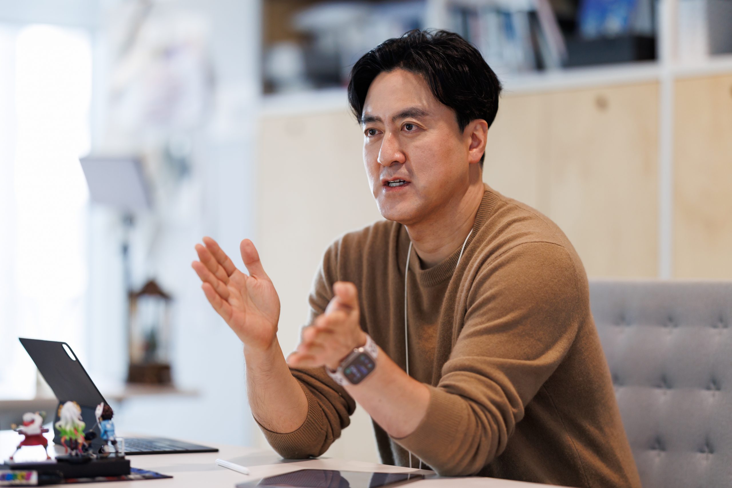 브라운 스웨터를 입은 남성이 제스처를 취하며 이야기하는 모습